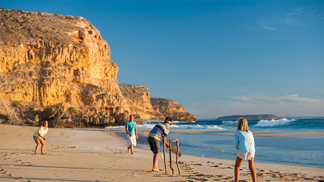 Family playing cricket on the beach.